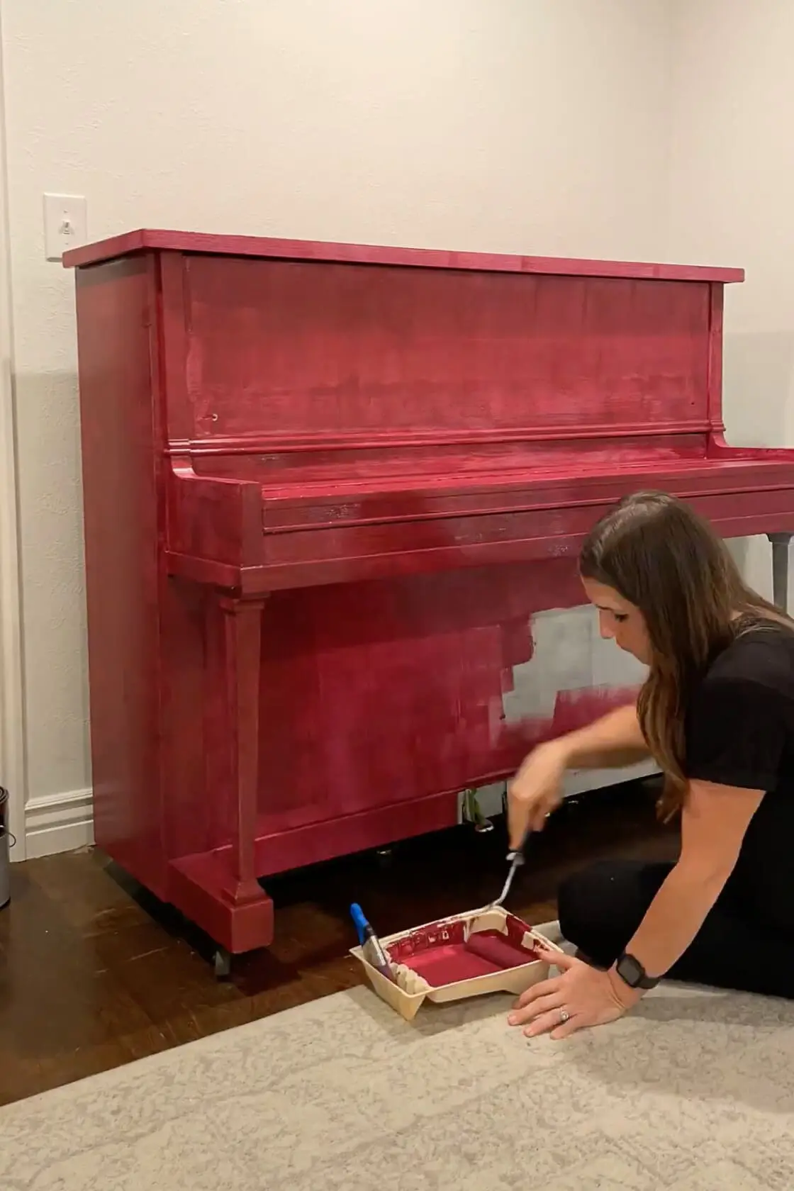 A partially painted upright piano with the first coat of deep burgundy paint being applied, transforming the old wooden piece into a bold statement.